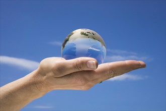 Woman's hand holding a glass globe against a blue sky