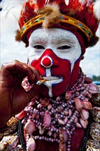 Man in a colourfully decorated costume with face paint smoking a cigarette at the traditional sing-sing gathering
