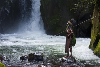 Decorated and painted tribal chief standing in front of a waterfall in the Highlands