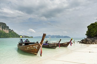 Three longtail boats on a white sandy beach