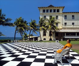Monk sitting on a bench on a mosaic terrace in the garden in front of the Galle Face Hotel
