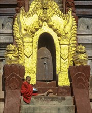 Monk sitting on a staircase at the door of Shwezigon Pagoda with its golden chedi