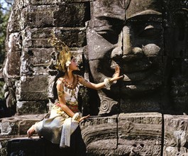 Temple dancer or apsara sitting in front of a face tower at Bayon Temple