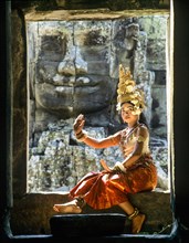 Temple dancer or apsara sitting in a window in front of a face tower at Bayon Temple