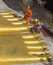 Monk praying at the feet of the golden Buddha statue of Wat Intharawihan