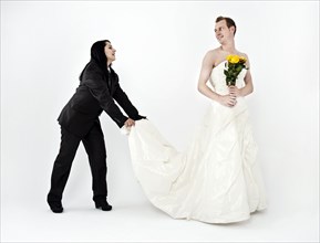Bride wearing a suit while holding the train of a wedding dress worn by the groom