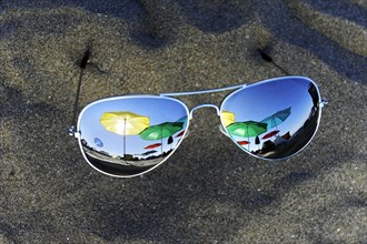Parasols are reflected in sunglasses lying in the sand