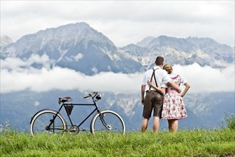 Man and a woman wearing traditional costume with an old bicycle looking towards the mountains
