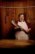 Fat butcher holding a meat cleaver in a butcher's store with a wooden ambience