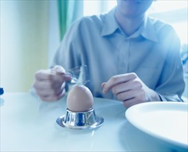 Man sitting at a table and tapping a boiled egg with a spoon