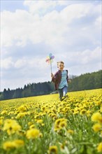 Boy running with colorful pinwheel on dandelion meadow