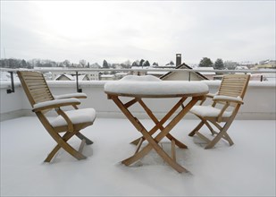 Two snow-covered chairs and a snow-covered table on a terrace