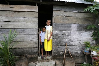 Girl and elderly woman standing at the entrance of her hut in a poor village