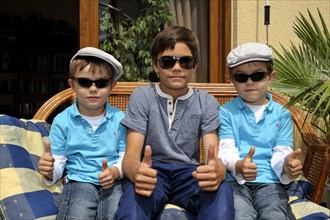 Twins and their older brother sitting together on a bench on a terrace