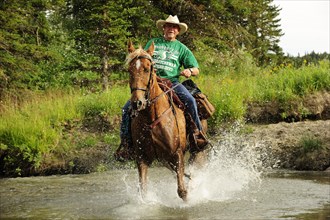 Cowboy riding through a river with splashing water
