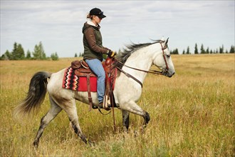 Woman riding on a gray horse across the prairie