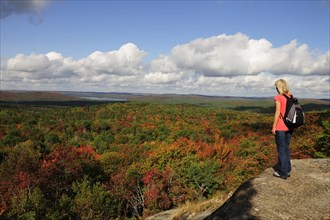 Female hiker standing on a rock overlooking a colourful autumnal forest