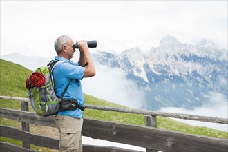 Hiker looking at the Tannheim mountains with binoculars