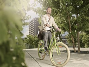 Man carrying a bag over his shoulder while riding a bicycle in the park