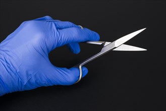 A hand with a blue medical glove is holding a pair of scissors