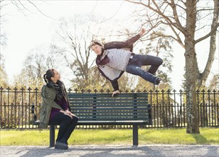 Young man trying to impress indifferent girl by jumping over a park bench