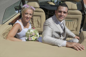 Bride and groom posing in the back seat of an open car