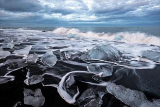 Pieces of ice on black beach lapped by the sea