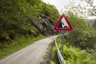 Falling rocks warning sign by narrow mountain road