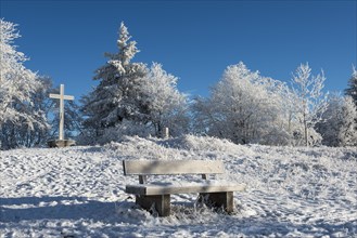Snow-covered bench and summit cross on the Gaisberg