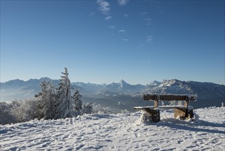 Snow-covered bench in front of Alpine panorama