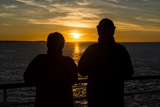 Couple at the railing of a ship watching the sunset on the North Atlantic coast of Thurso