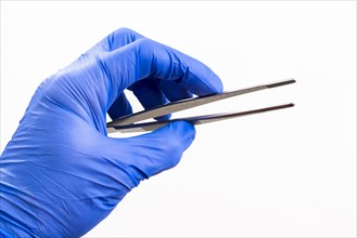 A hand with a blue medical glove is holding tweezers