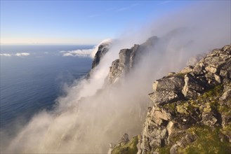 Fog falls down a steep cliff to the sea