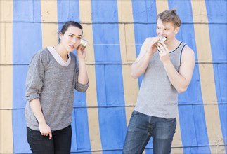 Young man talking into a tin can phone and young woman listening