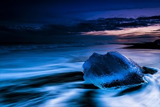 Chunk of ice on black lava sand beach at the blue hour