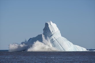 Pieces breaking off an enormous iceberg causing it to unbalance and collapse