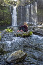 Young woman sitting on a stone in a river