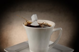 Two sugar cubes falling into a cup of coffee