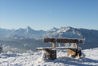 Snow-covered bench in front of Alpine panorama