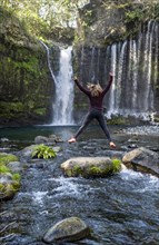 Young woman jumps into the air on a stone in a river