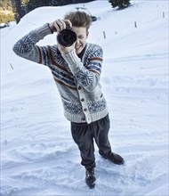 Young man in the snow taking a picture with a digital SLR camera