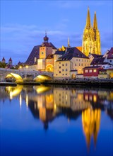 Illuminated Old Town with Stone Bridge and Cathedral reflected in the Danube at dusk