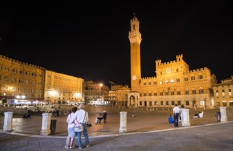 Tourists at the Palazzo Pubblico with illuminated Mangia Tower and chapel