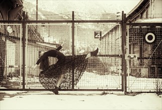 Dancer in a black dress performing in front of an old fence in winter