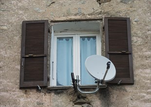 Window in a dilapidated building with satellite dish and open shutters