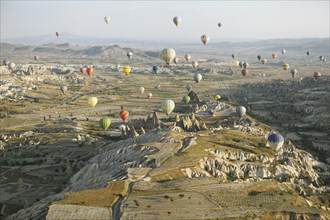 Hot air balloons rising over the cave dwellings and tufa formations in the morning light