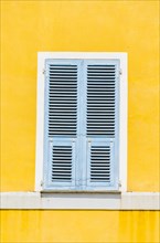 Yellow plastered wall with closed bright blue wooden shutters