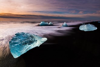 Chunks of ice on black lava sand beach at sunrise