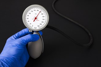 A hand with a blue medical glove is holding a sphygmomanometer