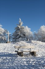 Snow-covered bench and summit cross on the Gaisberg